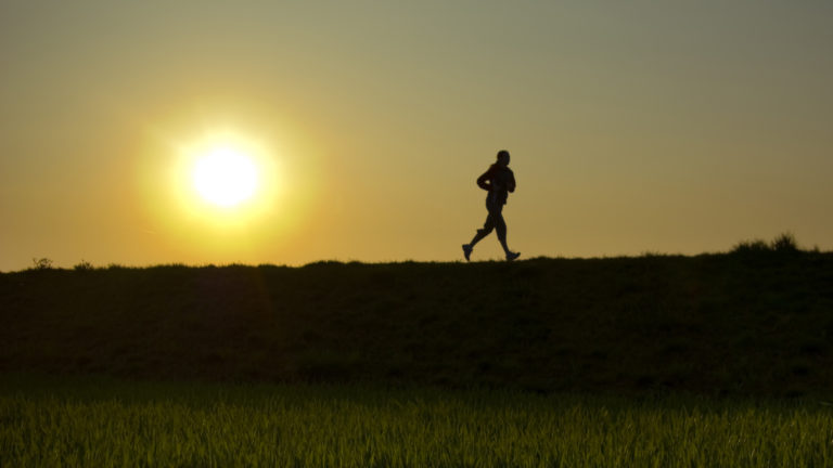 Mann läuft auf Wiese mit Sonnenuntergang im Hintergrund